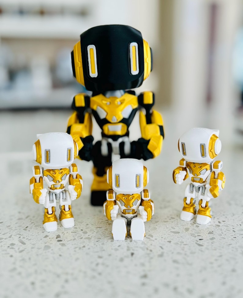 May include: A collection of four robot figurines. One large robot features a black head with white rectangular eyes, a gold and black torso, and gold arms. Three smaller robots feature white heads with gold accents, white torsos, and gold limbs.