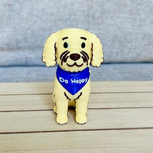 May include: A light yellow dog figurine with floppy ears and brown facial details. The dog wears a bright blue triangular bandana around its neck with the white text Do Happy printed clearly on the front. The figure is rendered in a smooth finish.