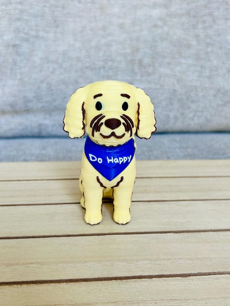 May include: A light yellow dog figurine with floppy ears and brown facial details. The dog wears a bright blue triangular bandana around its neck with the white text Do Happy printed clearly on the front. The figure is rendered in a smooth finish.