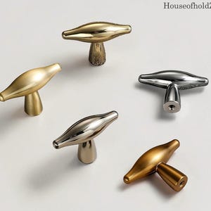 May include: A selection of metallic cabinet knobs in gold and silver finishes. The knobs feature a distinctive T-shape design with a rounded, elongated top and a textured or smooth base. The brand name "HouseofholdZ" is visible in the top right corner.