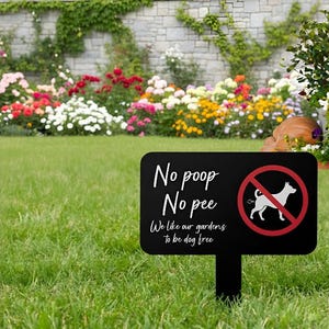 May include: A black garden sign with the text "No poop No pee" and a dog symbol inside a red circle with a line through it. The sign is in a grassy garden with a flower bed in the background.