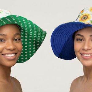 Puede incluir: Dos mujeres con sombreros para el sol. Uno tiene un ala verde con lunares y lazos, el otro tiene un ala azul y un estampado de girasoles. Los sombreros están diseñados para la protección solar.