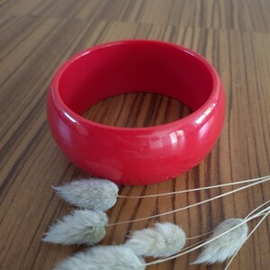 Peut inclure: Un bracelet jonc rouge vif et uni, doté d'une finition lisse et brillante ainsi que d'un profil épais et arrondi. Cet accessoire circulaire présente un design à large bande qui conserve une couleur uniforme sur toute sa surface extérieure.