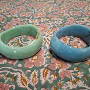 Peut inclure: Deux bracelets joncs épais et arrondis avec une finition lisse et polie. L'un est d'un vert menthe pâle et doux, tandis que l'autre est d'un bleu ciel éclatant. Les deux pièces présentent de subtils motifs marbrés tourbillonnants.