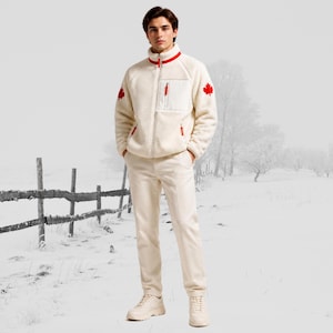 Puede incluir: Una chaqueta de forro polar color crema con cremallera, cuello alto, ribetes rojos y parches de hoja de arce roja en las mangas. La chaqueta cuenta con un bolsillo en el pecho con tirador rojo. Se combina con pantalones color crema y zapatillas blancas.