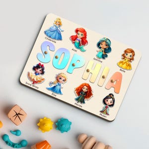 May include: Wooden puzzle featuring the name "SOPHIA" with colorful letters and illustrations of Disney princesses. Includes Cinderella, Ariel, Jasmine, Belle, Snow White, Elsa, Merida, and Mulan. A fun educational toy for children.