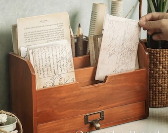 May include: A wooden desk organizer with multiple compartments and a drawer. The organizer is stained a warm brown color and filled with vintage papers, pencils, and rolled documents. The text "Organika Wood" is printed on the front.