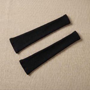 May include: Two black, ribbed knit arm warmers. The arm warmers are made of a soft, stretchy material and have a fitted design. They are designed to be worn on the arms, covering the wrists and forearms.