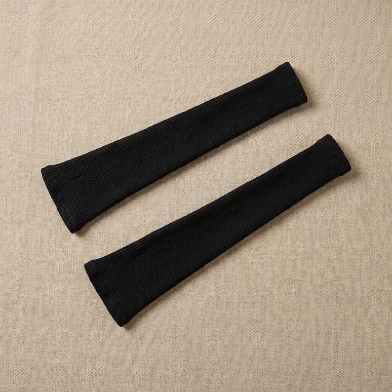May include: Two black, ribbed knit arm warmers. The arm warmers are made of a soft, stretchy material and have a fitted design. They are designed to be worn on the arms, covering the wrists and forearms.