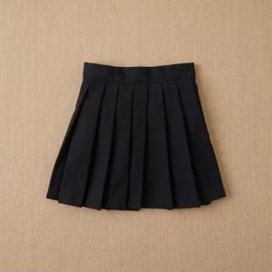May include: A black pleated skirt, viewed from above, against a neutral background. The skirt has a classic A-line shape with evenly spaced pleats. The fabric appears to be a solid, opaque material.