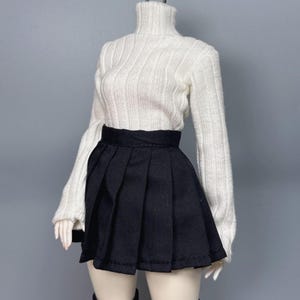 May include: A doll-sized outfit featuring a white ribbed turtleneck sweater and a black pleated mini skirt. The sweater has long sleeves. The skirt has a wide waistband and a flared silhouette. The outfit is displayed on a doll.