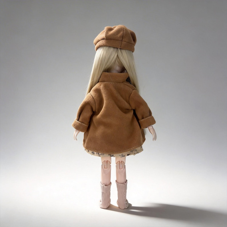 K&ouml;nnte beinhalten: Eine Puppe mit langen blonden Haaren, die einen braunen Mantel, einen passenden Hut und hellrosa Stiefel tr&auml;gt. Das Kleid der Puppe hat ein Blumenmuster. Die Puppe steht mit dem R&uuml;cken zum Betrachter.