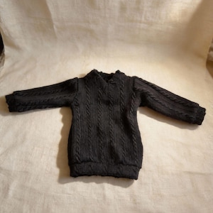 Pu&ograve; includere: Un maglione nero a trecce con maniche lunghe. Il maglione ha uno scollo tondo e un motivo strutturato sul corpo e sulle maniche. L'indumento &egrave; esposto su uno sfondo neutro.