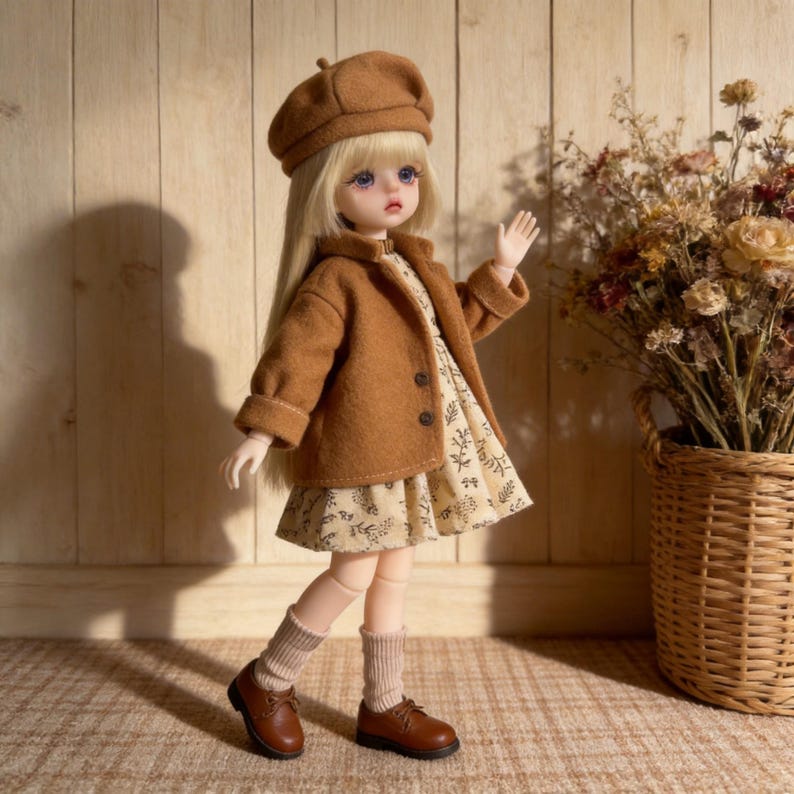 K&ouml;nnte beinhalten: Eine Puppe mit braunem Barett, Jacke und Kleid mit floralem Muster. Die Puppe hat lange blonde Haare, braune Schuhe und beige Socken. Im Hintergrund befindet sich ein Korb mit Trockenblumen.