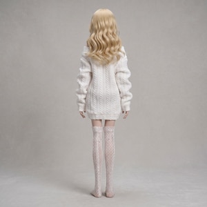 Puede incluir: Una mu&ntilde;eca con cabello rubio largo y ondulado que viste un vestido tipo su&eacute;ter blanco de punto trenzado y medias blancas estampadas hasta el muslo. La mu&ntilde;eca se ve desde atr&aacute;s, mostrando el patr&oacute;n de punto del su&eacute;ter y el dise&ntilde;o de encaje de las medias.