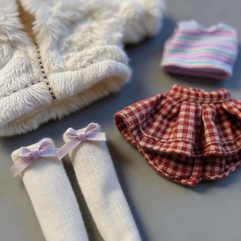 May include: A doll clothing set featuring a white fuzzy jacket, a striped top, a red and white checkered skirt, and white socks with pink bows. The miniature outfit is designed for a doll.