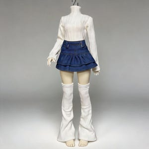 May include: A white ribbed turtleneck sweater paired with a denim mini skirt and white leg warmers. The skirt has a layered ruffle design. The outfit is displayed on a mannequin against a neutral background.
