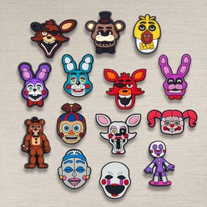 May include: A collection of colorful cartoon character charms, featuring various designs with distinct facial expressions and features. The charms are in various colors, including red, blue, yellow, purple, and brown.