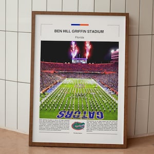 May include: Framed print of Ben Hill Griffin Stadium in Florida. The image shows a night view of the stadium with fireworks and a marching band on the field. The word "Gators" is prominently displayed.