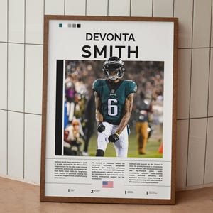 May include: A framed poster featuring Devonta Smith in an Eagles uniform. The poster includes his name, number 6, and biographical text. The frame is brown, and the background is a football field.