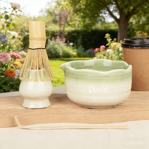 May include: A white ceramic mug with a black handle and the text "But First, Coffee" in a black, handwritten-style font. The mug is on a white surface.