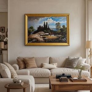 May include: An oil painting in a gold frame depicts a landscape with trees, a hill, and a cloudy sky. The painting hangs above a beige sofa with decorative pillows. A wooden coffee table and side table are in front of the sofa.