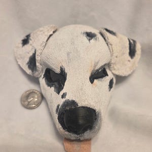 May include: A handmade Dalmatian dog head sculpture. The dog's head is white with black spots, black eyes, and a black nose. A small, pink tongue is sticking out. A US quarter is next to the sculpture for size comparison.