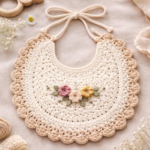 May include: A cream-colored, crocheted baby bib with a scalloped edge and a tie closure. The bib features embroidered flowers in pink, yellow, and cream, with green leaves. The bib is made of soft yarn.