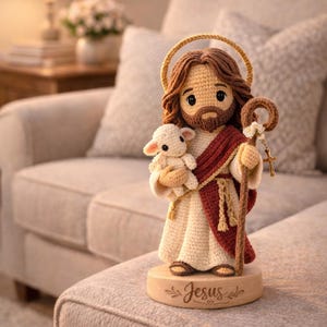 May include: A handcrafted crochet figurine of Jesus holding a lamb, with a halo and staff. The figure is dressed in cream and burgundy robes, standing on a wooden base with the word "Jesus" engraved. The overall design is soft and inviting.