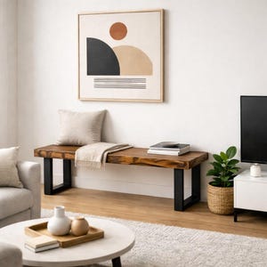 Può includere: Una panca in legno con finitura naturale e gambe in metallo nero. Una coperta e un cuscino beige poggiano sulla panca. Un'opera d'arte astratta incorniciata è appesa al muro sopra la panca.