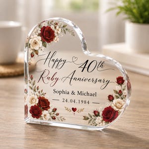 May include: A heart-shaped clear acrylic plaque featuring a floral design of red and white roses. The text reads: Happy 40th Ruby Anniversary, Sophia & Michael, 24.04.1984. The design includes a small heart icon and decorative greenery accents.