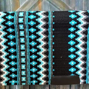 May include: A rectangular horse saddle pad featuring a woven pattern in black, bright turquoise, and grey. The design consists of vertical stripes with geometric diamond and zigzag motifs. A solid black leather patch is located at the bottom corner.