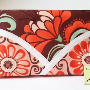 May include: A brown, white, and orange floral print zippered pouch with a white trim. The pouch has a "cozy nest design" logo in the bottom right corner.