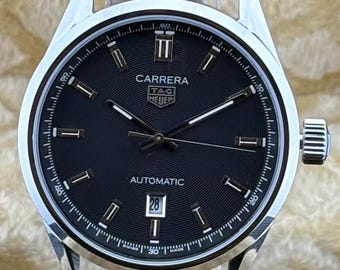 Reloj de pulsera vintage Tag Heuer con movimiento automático, esfera negra, correa de cuero negra, fondo transparente, fecha funcional y caja de acero inoxidable para hombre.