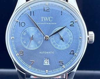 Reloj de hombre IWC PORTUGIESER automático vintage con reserva de marcha de 7 días, esfera azul cielo, correa de cuero, caja plateada, fecha funcional y fondo transparente.