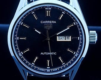 Reloj de hombre Tag Heuer Carrera vintage con movimiento automático, esfera negra, correa de cuero negra, fondo transparente, fecha/día funcional, acero inoxidable.