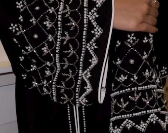 May include: Black garment with intricate white beaded embellishments on the sleeves and front. The design features floral and geometric patterns, with a white trim along the edges. The sleeves are long and the garment appears to be made of a flowing fabric.
