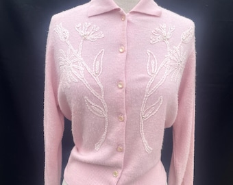 May include: A light pink long-sleeve cardigan featuring a collared neckline and a front button closure. The garment is decorated with tonal embroidered floral patterns on both sides of the chest, accented with small beads throughout the design.