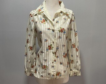 Puede incluir: Una camisa vintage de botones de manga larga, de color crema, con estampado floral y rayas verticales. La camisa tiene cuello y mangas largas con puños de botón.