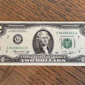 May include: A United States two-dollar banknote. The note features a portrait of Thomas Jefferson and the text "TWO DOLLARS". The bill is green and black with the serial number G 84096041 A.
