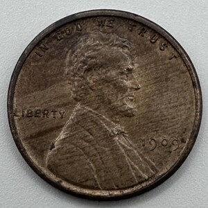 Puede incluir: Una moneda de cobre Lincoln de 1909. El anverso presenta un perfil de Abraham Lincoln, la palabra "LIBERTY" y la inscripción "IN GOD WE TRUST". El año "1909" es visible.