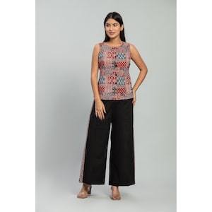 May include: A sleeveless top featuring a multi-colored patchwork pattern in shades of red, blue, and white, paired with black wide-leg trousers that have a matching patterned fabric strip running down the outer side of each leg.