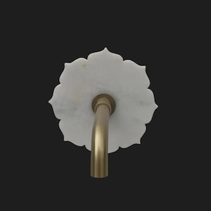May include: A white marble flower-shaped sink tap with a curved, gold-coloured spout. The tap is set against a black background, highlighting its elegant design. The fixture is a decorative element for a bathroom.