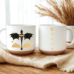 May include: Two white ceramic mugs with brown bottoms. One mug features a black dragon design with gold accents. The other mug has a series of gold dragon silhouettes. Both mugs have a curved handle.