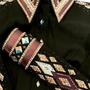 Könnte beinhalten: Schwarzes Westernhemd mit aufwendigen Verzierungen. Kragen und Manschetten weisen ein geometrisches Design mit Strasssteinen, Kristallen und metallischen Akzenten auf. Der Text "WARDA WESTERN STORE" ist unten im Bild zu sehen.