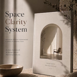 Op de afbeelding: Een boek getiteld "Space Clarity System" met informatie over het interieurontwerpframework. De omslag heeft een boogontwerp met een stoel en een vaas binnenin. De tekst luidt "Design spaces that truly hold you."