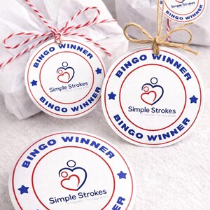 May include: White round "Bingo Winner" tags with red and blue text and star accents. The tags feature the "Simple Strokes" logo and are attached to wrapped gifts with twine and red and white string.