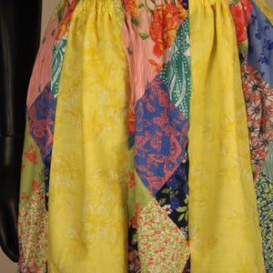 May include: A colorful patchwork skirt with a yellow background and panels of floral and geometric patterns in various colors. The skirt has an elastic waistband and a flowing silhouette, perfect for a summer outfit.