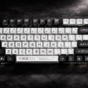 May include: A mechanical keyboard with white and black keycaps. The keys are arranged in a standard QWERTY layout. The keyboard has a black base and features various function keys and special keys.