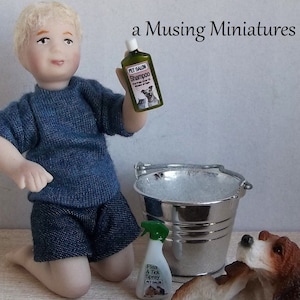 May include: A miniature dollhouse scene with a boy doll kneeling beside a small dog doll. The boy is holding a bottle of pet shampoo and the dog is near a small silver bucket and a bottle of flea and tick spray. The scene is set on a wooden surface.